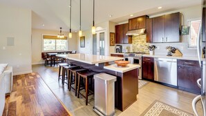 A modern kitchen with a central island, stainless steel appliances, and wooden bar stools. - Kona Coast Hideaway w/ Patio & Pacific Ocean Views (Kailua-Kona)