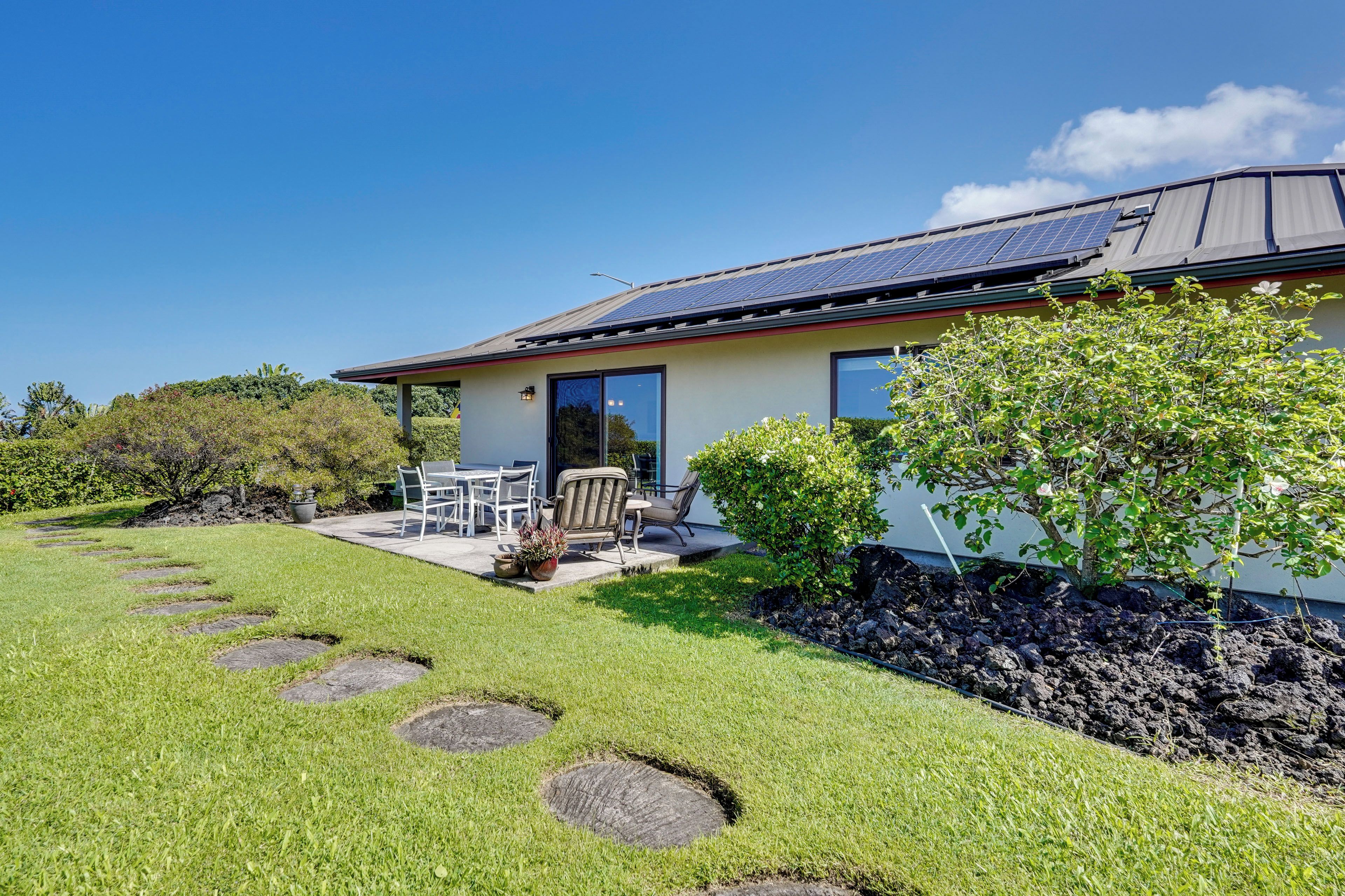 A modern house with a solar panel roof, a patio with outdoor furniture, and a well-maintained garden.