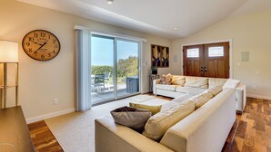 A spacious living room with a large sofa, a clock, and a sliding glass door leading to an outdoor area. - Kona Coast Hideaway w/ Patio & Pacific Ocean Views (Kailua-Kona)