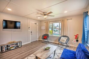 A modern living room with a flat-screen TV, a ceiling fan, a sofa, two armchairs, a coffee table, and a bookshelf.
