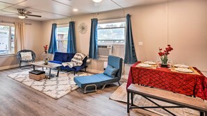 A modern living room with a sofa, a blue armchair, a small table with a vase of flowers, and a dining table set for two. - Cozy Elk Grove Home in the Heart of Old Town! (Elk Grove)