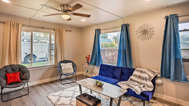 A living room with a blue sofa, two armchairs, a coffee table, a ceiling fan, and large windows with curtains. - Cozy Elk Grove Home in the Heart of Old Town! (Elk Grove)