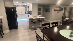 Une cuisine moderne avec un îlot central, un coin repas doté d’une table en bois foncé et un espace de vie comprenant un canapé et un tableau au mur.