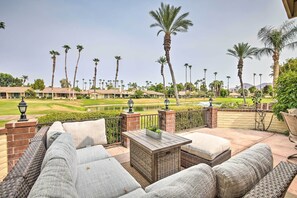 Eine Terrasse mit Korbmöbeln, einem kleinen Tisch und Blick auf einen Golfplatz und Palmen.