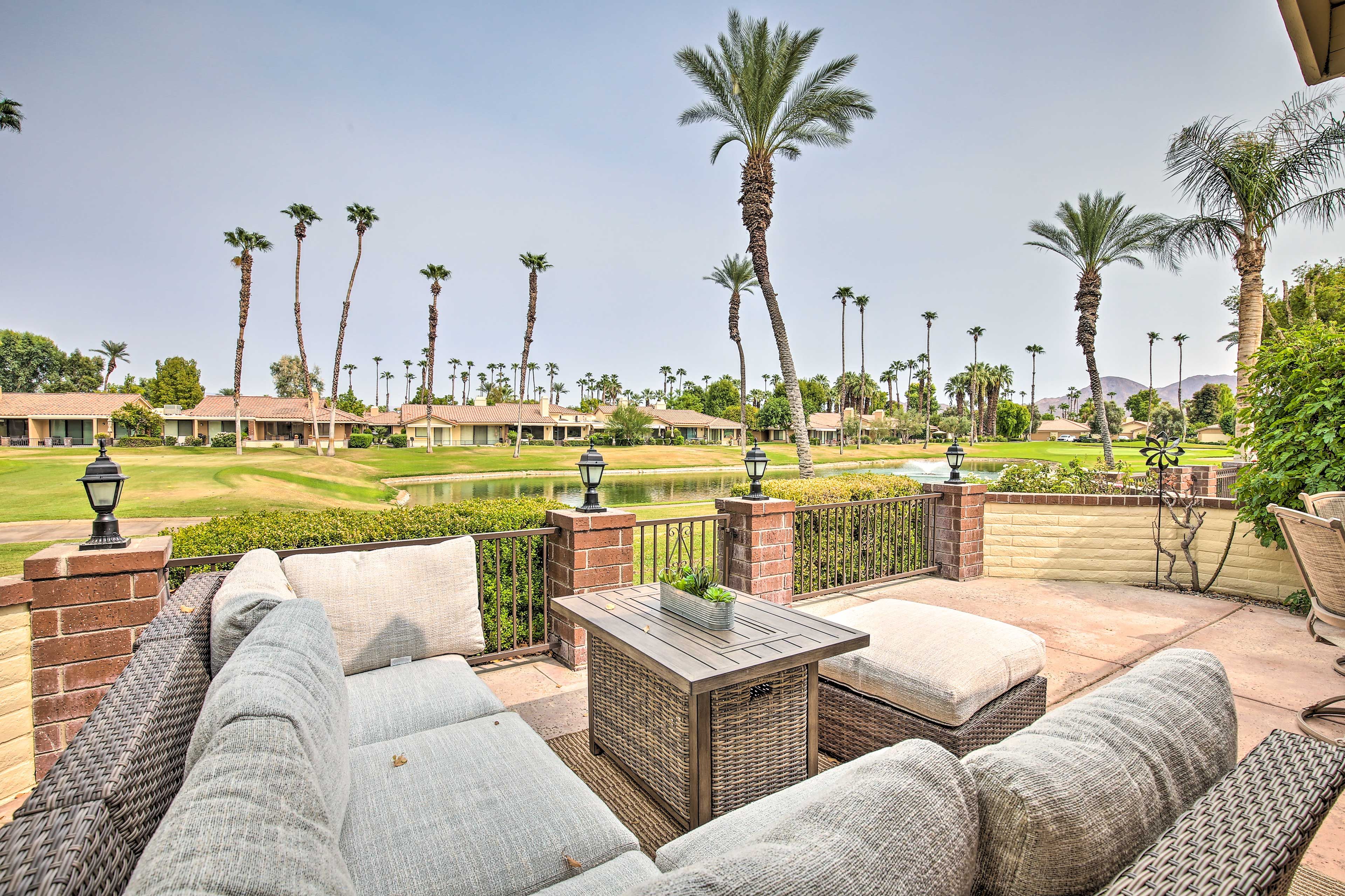 A patio with wicker furniture, a small table, and a view of a golf course and palm trees.