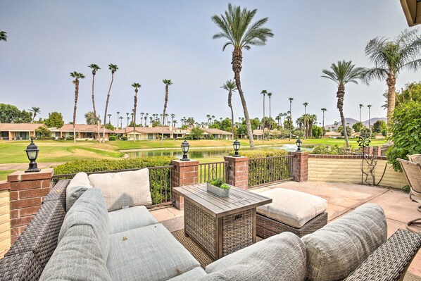 A patio with wicker furniture, a small table, and a view of a golf course and palm trees. - Palm Desert Escape w/ Patio & Shared Pool! (Palm Desert)