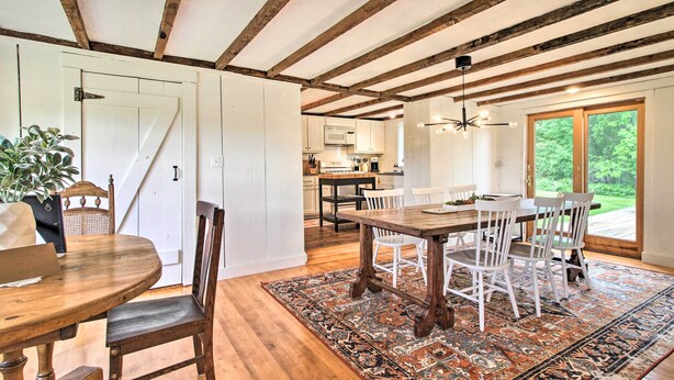 Un comedor con una mesa y sillas de madera, un tapete estampado y vistas al exterior a través de un ventanal.