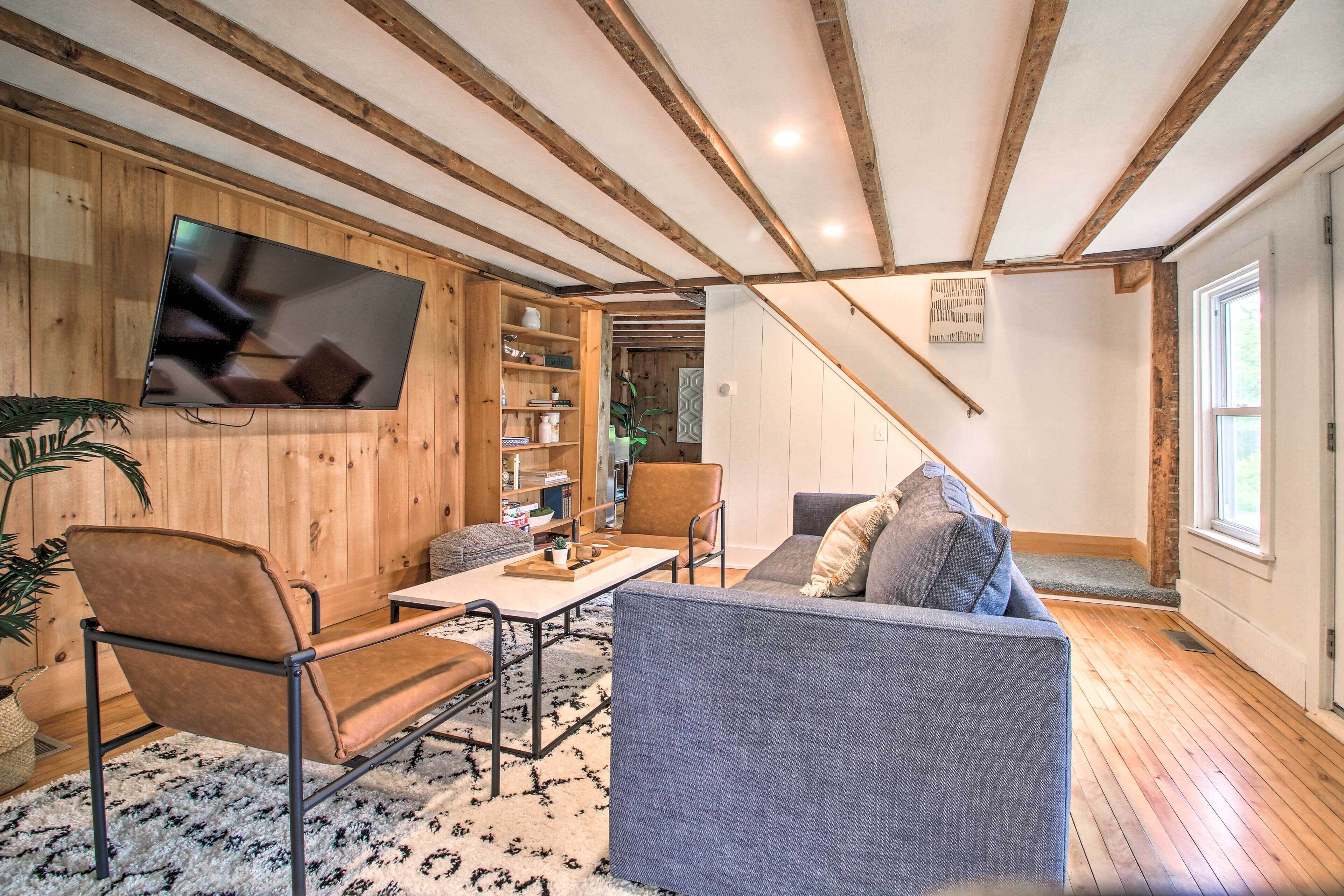 Una sala de estar acogedora con techo de madera, un televisor de pantalla plana montado en la pared, un sofá, una mesa de centro y una silla.