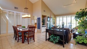 A spacious living area with a dining table, chairs, a sofa, and a coffee table. There is a large window providing natural light and a view of the outdoors.