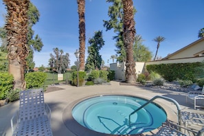 A swimming pool with a tiled edge, surrounded by palm trees and a patio area with lounge chairs.