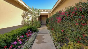 A narrow pathway flanked by lush greenery and vibrant flowers leading to a building entrance.
