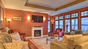 A cozy living room with a fireplace, large windows, and comfortable seating. - Stunning South Hero Home on Lake Champlain w/ View (South Hero)