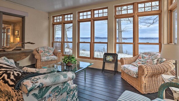 A cozy room with wicker furniture, large windows, and a view of a lake. - Stunning South Hero Home on Lake Champlain w/ View (South Hero)