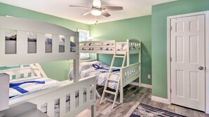 Une chambre d’enfant avec des lits superposés, un ventilateur de plafond et une porte.
