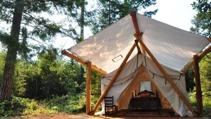 A tent with a bed inside, surrounded by a wooden deck and set in a forest.