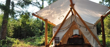 A tent with a bed inside, surrounded by a wooden deck and set in a forest.