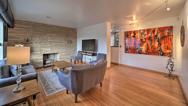 A modern living room with a fireplace, comfortable seating, a large abstract painting, and a wooden floor. - Tulsa Rental Home - Walk to Philbrook Museum (Tulsa)