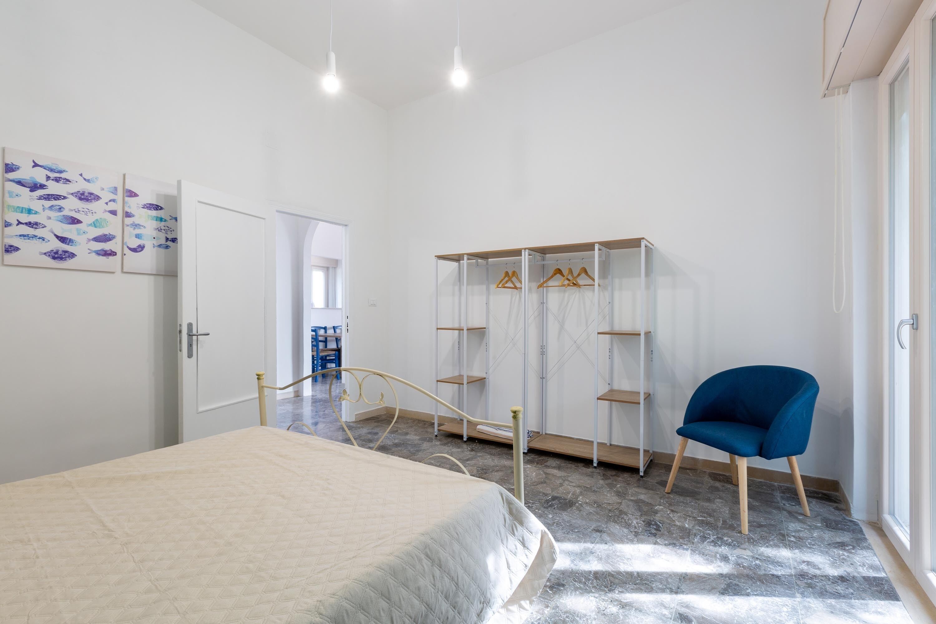 Un dormitorio con una cama, una silla azul, un armario y una puerta que da a otra habitación.
