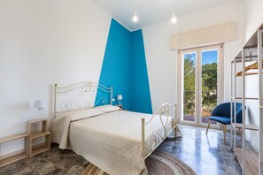 A bedroom with a bed, a nightstand, a chair, and a view of the outdoors.