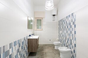 A bathroom with a white sink, wooden cabinet, two toilets, and a mirror.