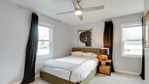 A bedroom with a bed, a ceiling fan, a nightstand, a lamp, and a window with curtains. - Charming Baltimore Getaway - 5 Miles to Downtown! (Baltimore)