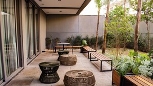 A patio area with round wicker tables and benches, surrounded by potted plants and trees. - Belint Paulista (São Paulo)