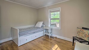Ein Schlafzimmer mit einem weißen Bett, einem kleinen weißen Nachttisch, einem Fenster mit Jalousien und Holzboden.