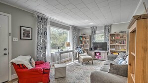 Ein Wohnzimmer mit einem roten Sofa, grauen Sesseln, einem Holzschrank und einem Bücherregal.