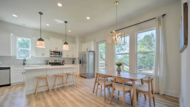 A modern kitchen with white cabinets, stainless steel appliances, wooden stools, and a dining table with chairs. - Canyon Lake Home w/ Deck ~ 1 Mi to Comal Park (Canyon Lake)