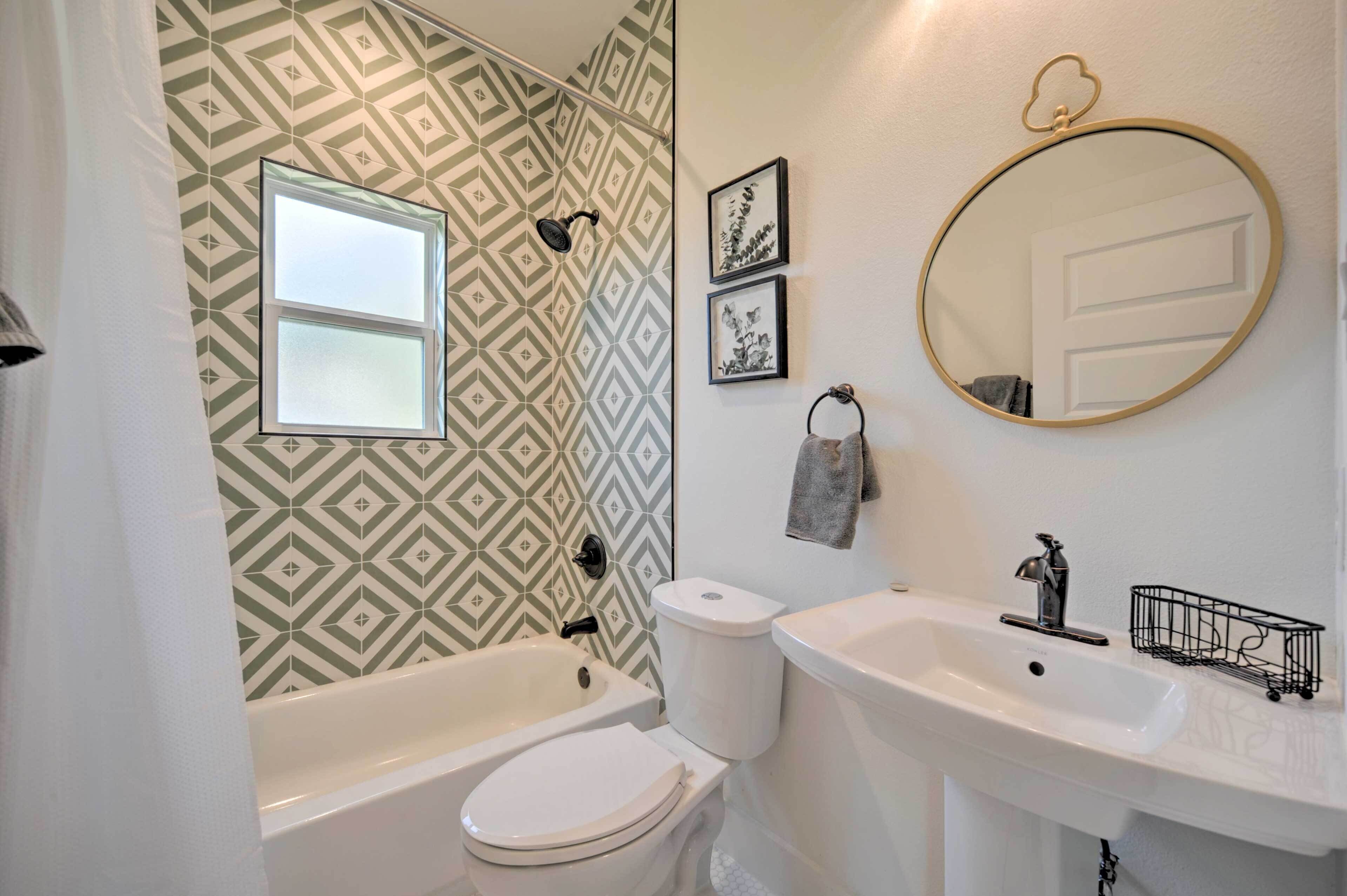 Une salle de bain avec un mur orné d’un motif géométrique, une fenêtre, des toilettes, une baignoire, un lavabo, un miroir et un porte-serviettes.