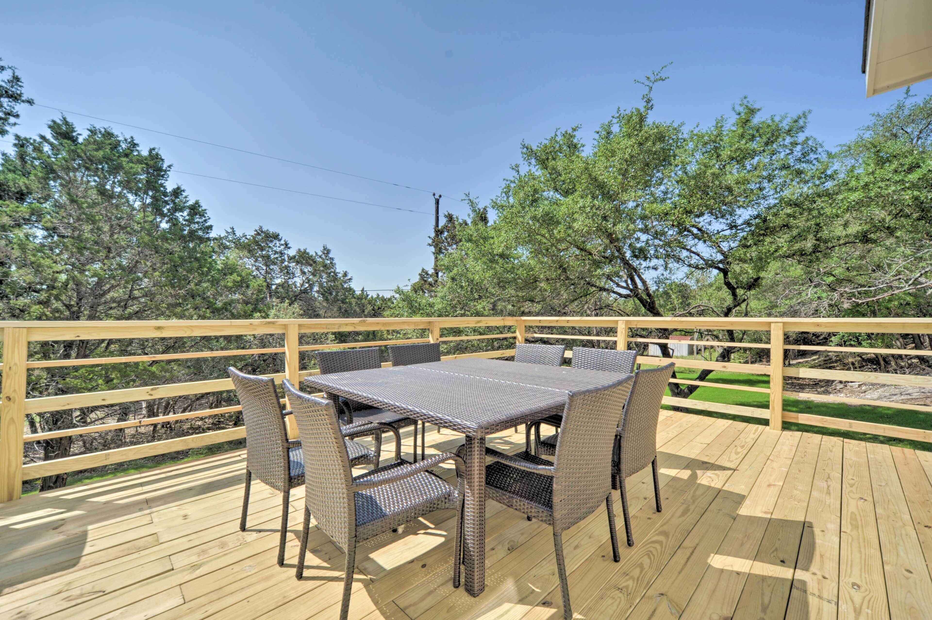 Una terraza de madera con una mesa y sillas, rodeada de árboles.