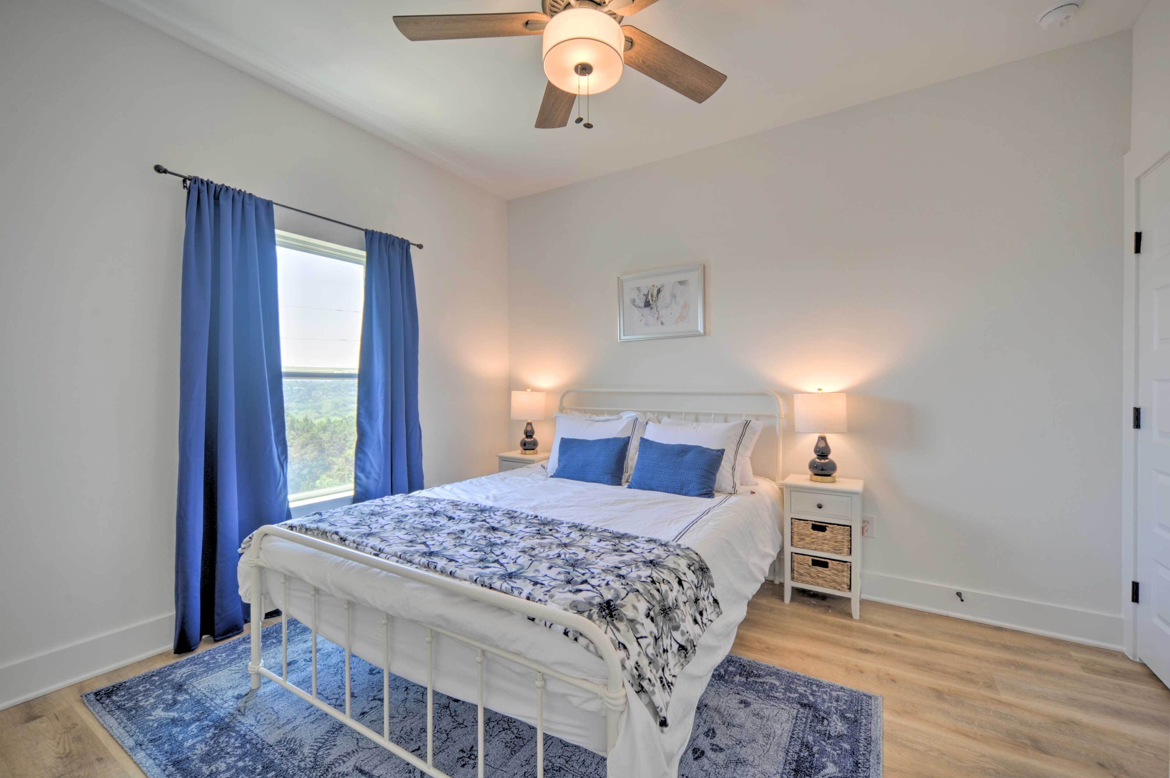 A bedroom with a bed, a ceiling fan, a nightstand with a lamp, and a window with curtains.