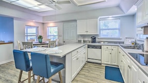 A modern kitchen with white cabinets, a central island, blue chairs, and a ceiling fan. - Bayfront Niceville Getaway w/ Private Dock! (Niceville)