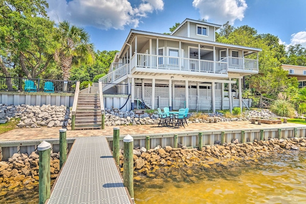 A two-story waterfront house with a balcony, a dock, and outdoor seating.