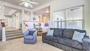 A living room with a grey sofa, a grey armchair, and a ceiling fan. There is a staircase leading to a kitchen and a dining area. - Bayfront Niceville Getaway w/ Private Dock! (Niceville)