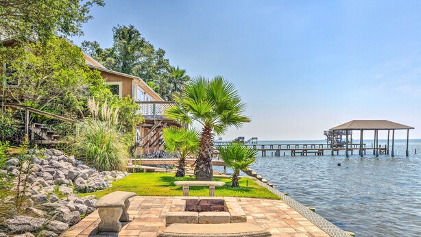 A waterfront patio with stone benches, a fire pit, and a view of the water and a pier. - Bayfront Niceville Getaway w/ Private Dock! (Niceville)
