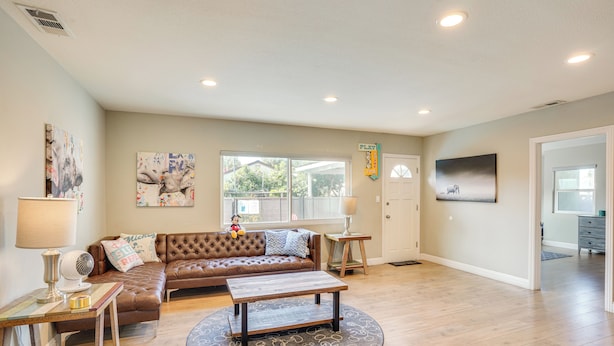 A spacious living room with a brown leather sofa, a wooden coffee table, and a large window. - Fullerton Vacation Rental w/ Private Pool! (Fullerton)