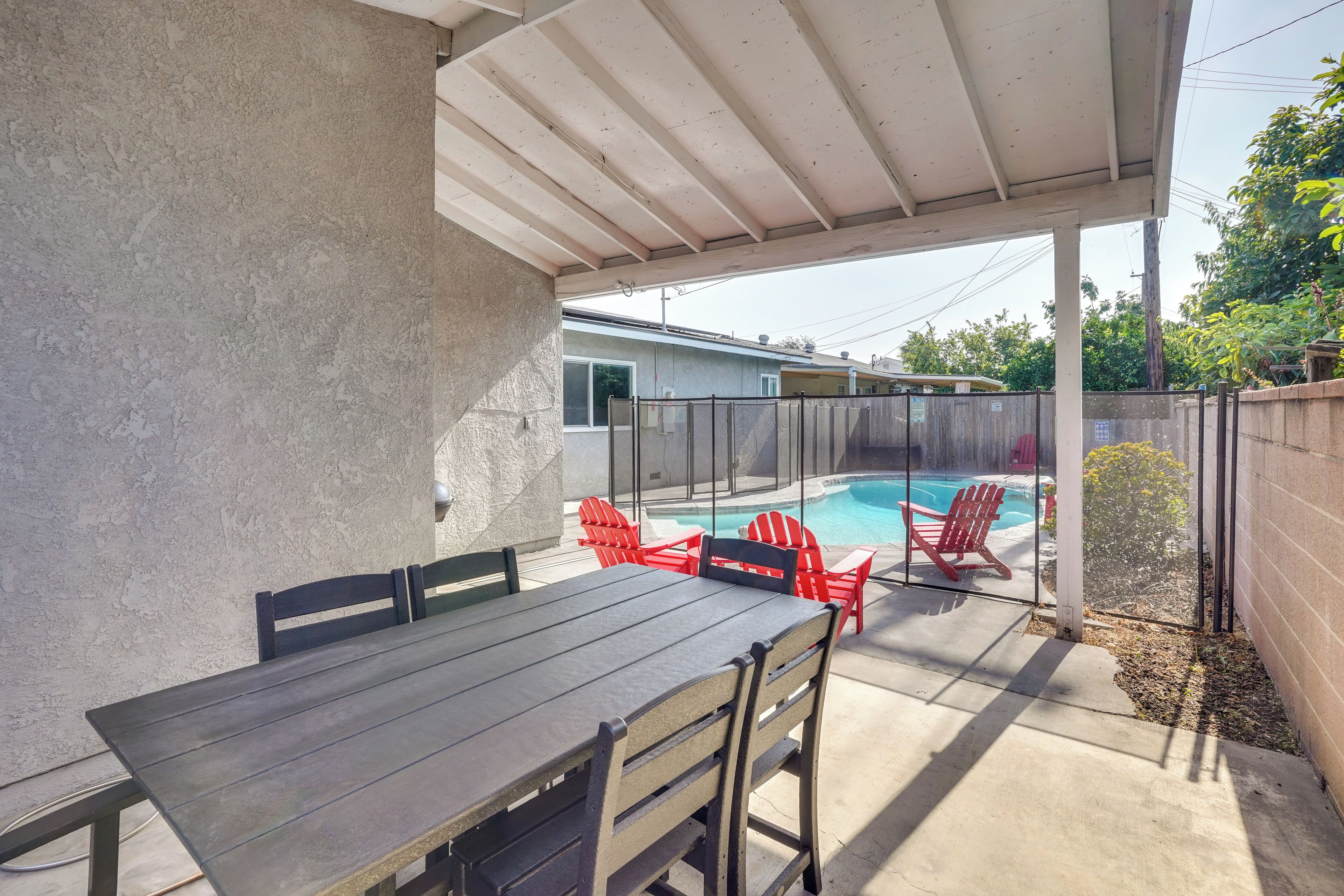 A covered patio with a pool, red chairs, and a table.
