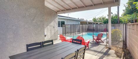 A covered patio with a pool, red chairs, and a table.
