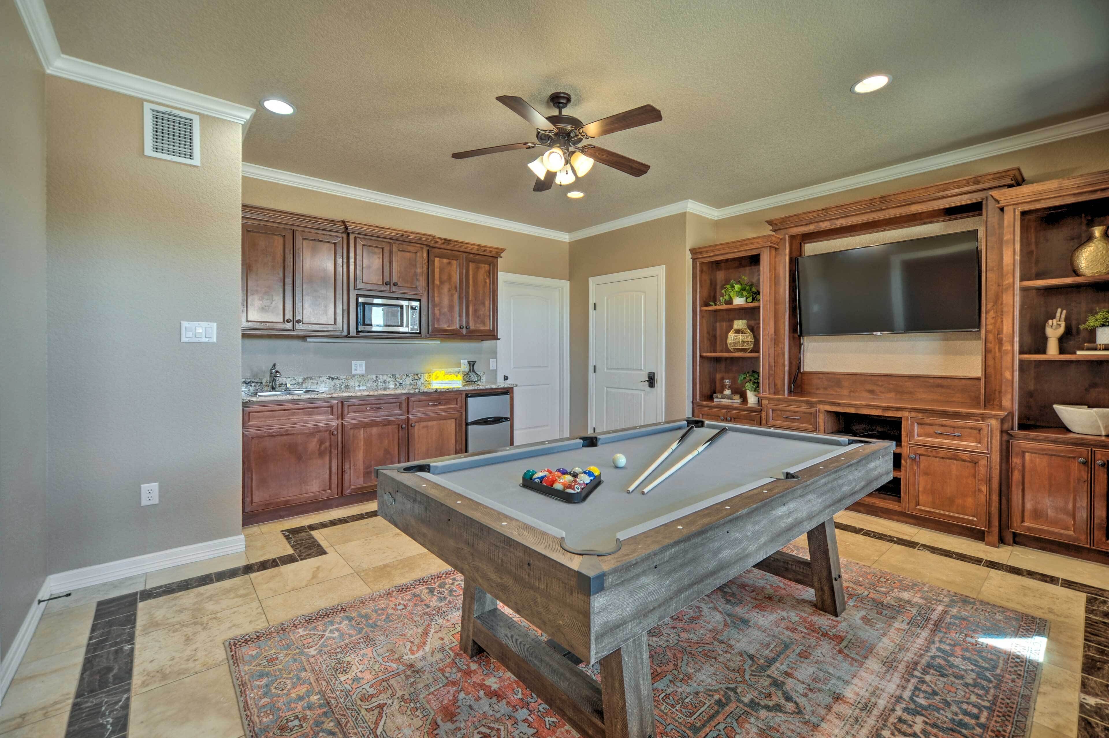 A pool table in a room with wooden cabinets, a microwave, and a television.