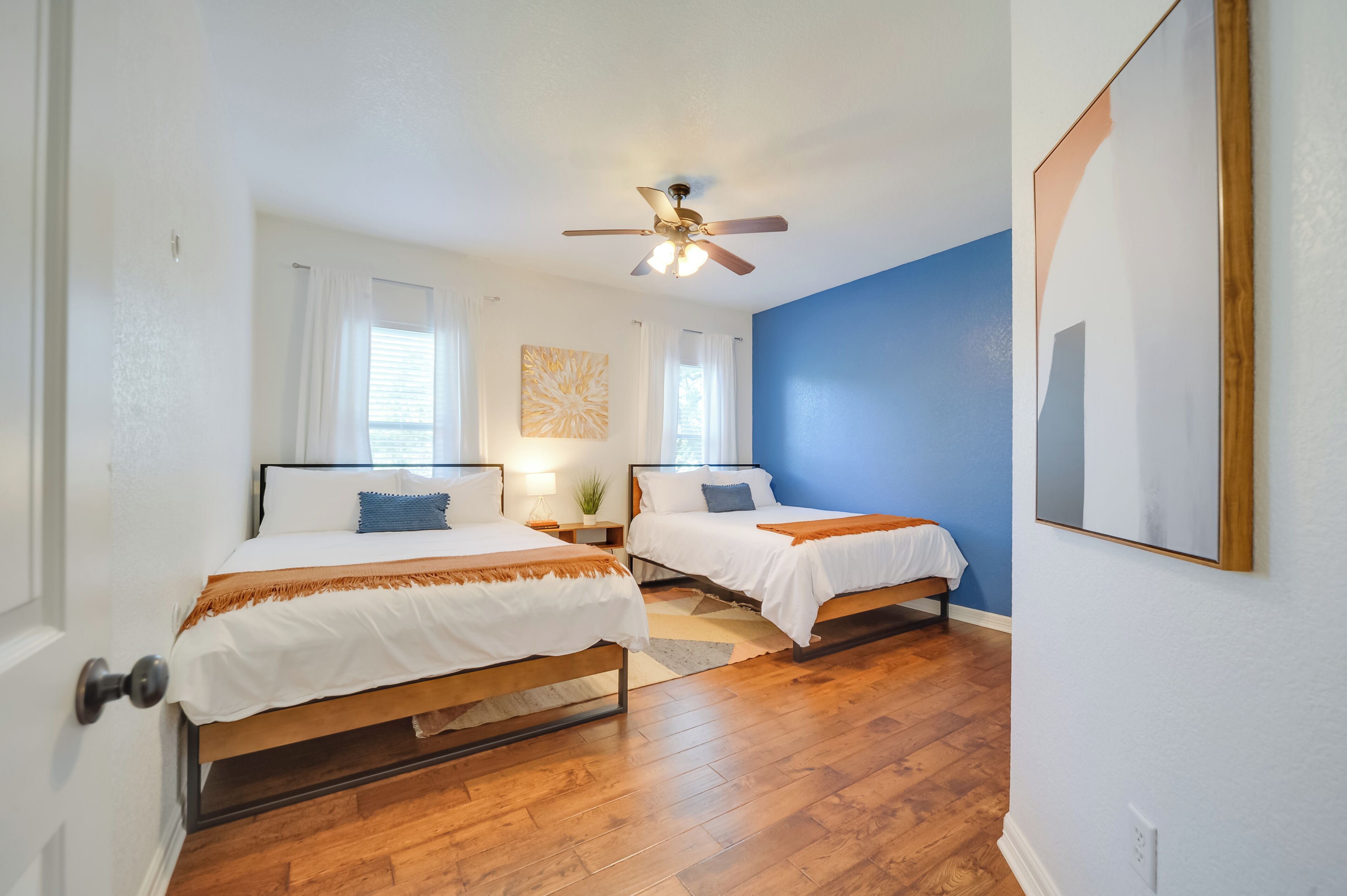 A bedroom with two beds, a ceiling fan, and a blue accent wall.
