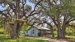 Una casa rústica con terraza de madera y una casita en un árbol.