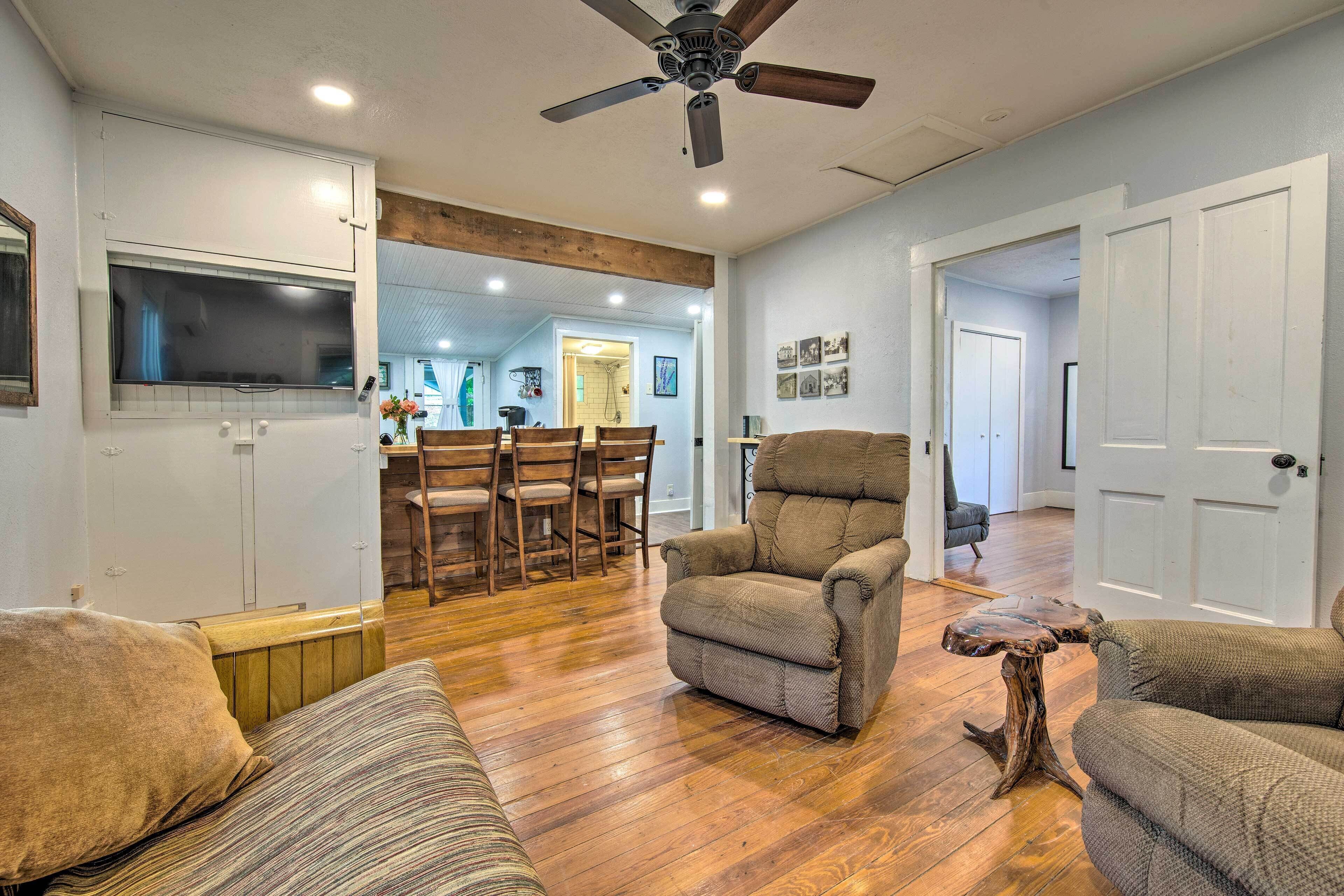 A spacious living room with a ceiling fan, wooden flooring, and a dining area with chairs and a table.