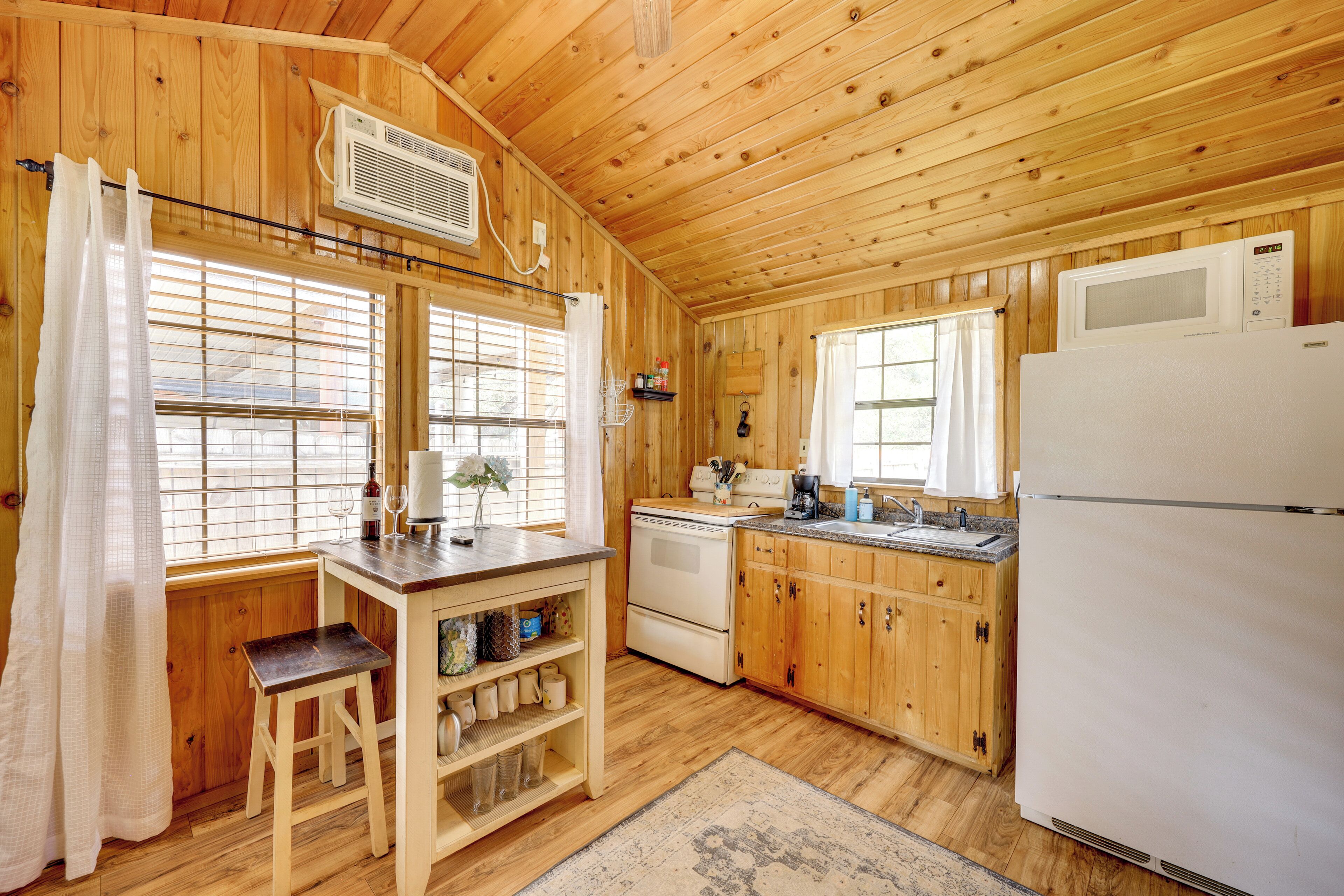A wooden cabin interior with a kitchen area, including a refrigerator, stove, and microwave.