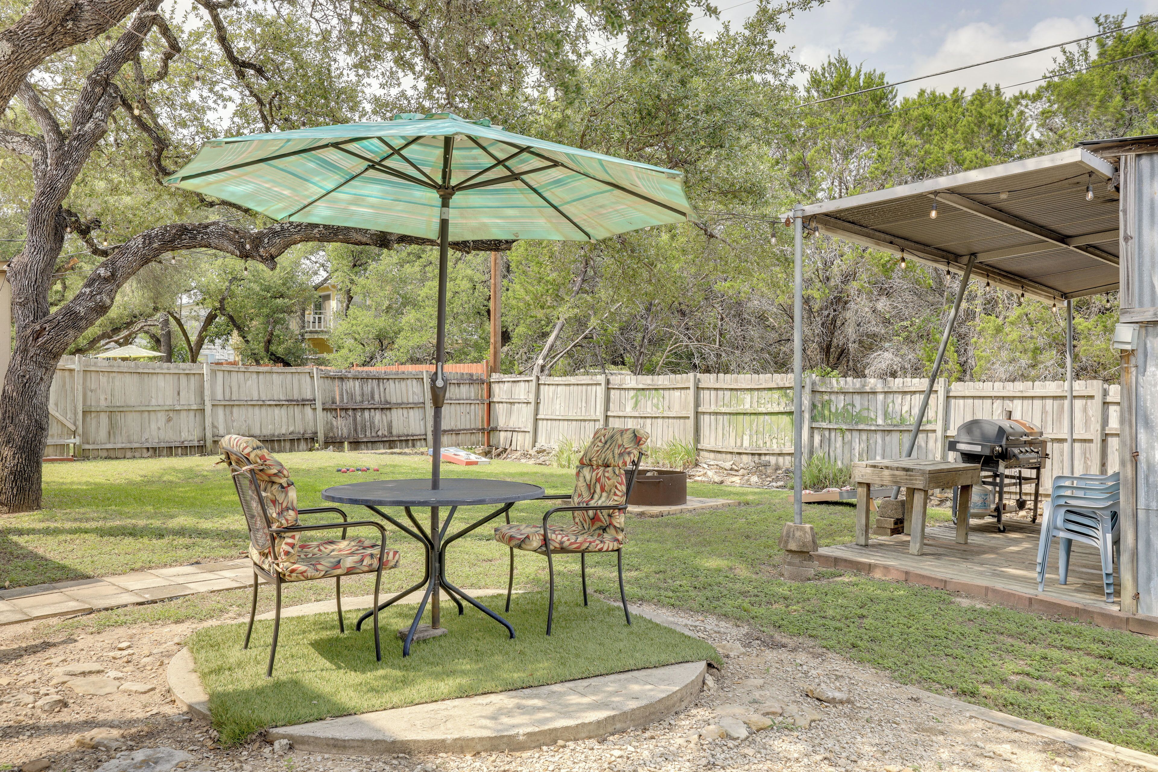 Un patio trasero con un espacio cubierto, una parrilla y una mesa con sillas.