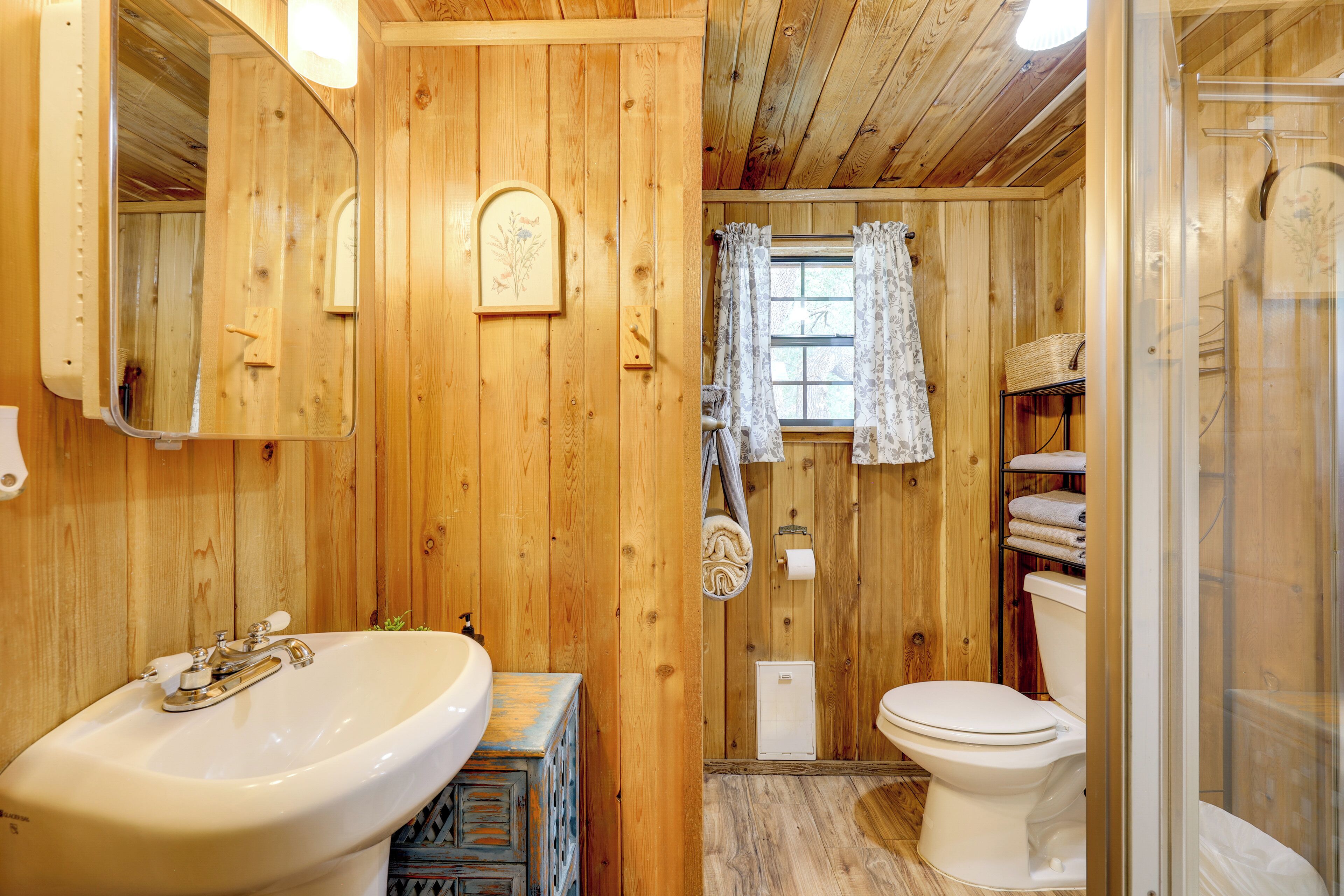 A wooden bathroom with a sink, toilet, and shower area.