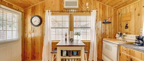 A wooden cabin interior with a kitchen, dining area, and a clock on the wall.