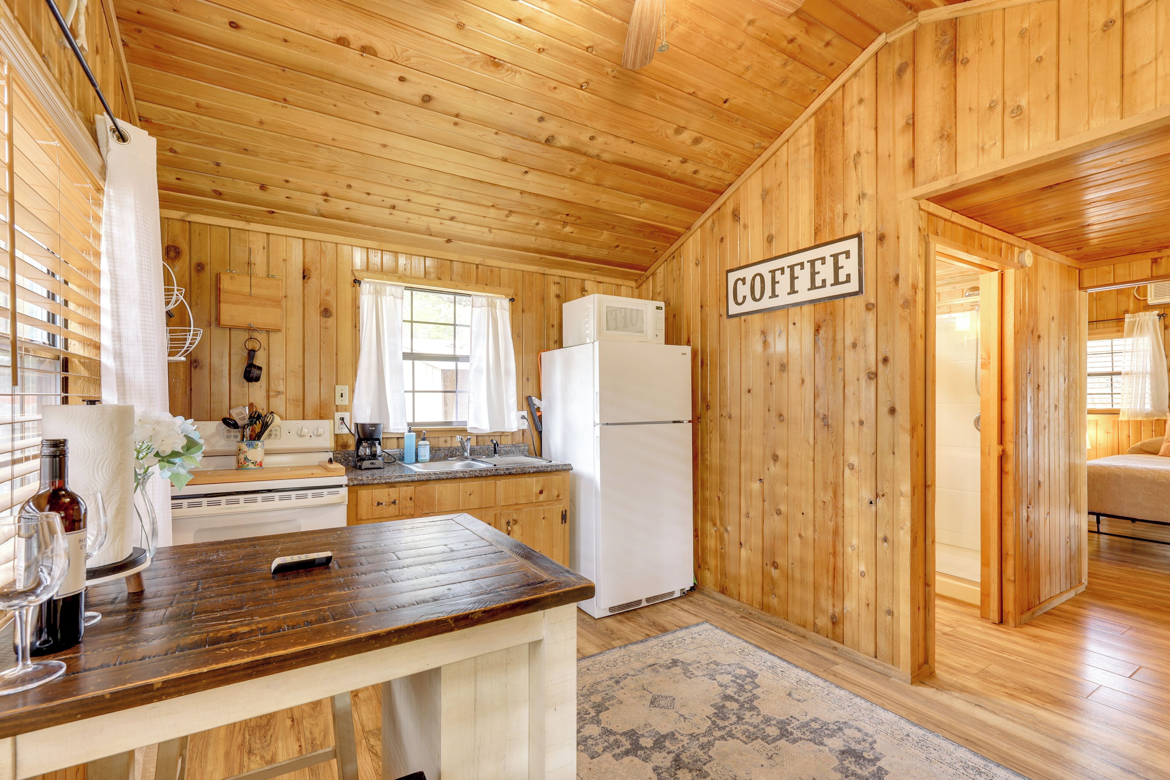 A wooden cabin interior with a kitchen area featuring a stove, sink, and refrigerator. A sign on the wall reads 'COFFEE.'