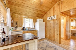 L’intérieur d’une cabane en bois comprend un coin cuisine équipé d’une cuisinière, d’un évier et d’un réfrigérateur. Un panneau sur le mur indique : « CAFÉ ».