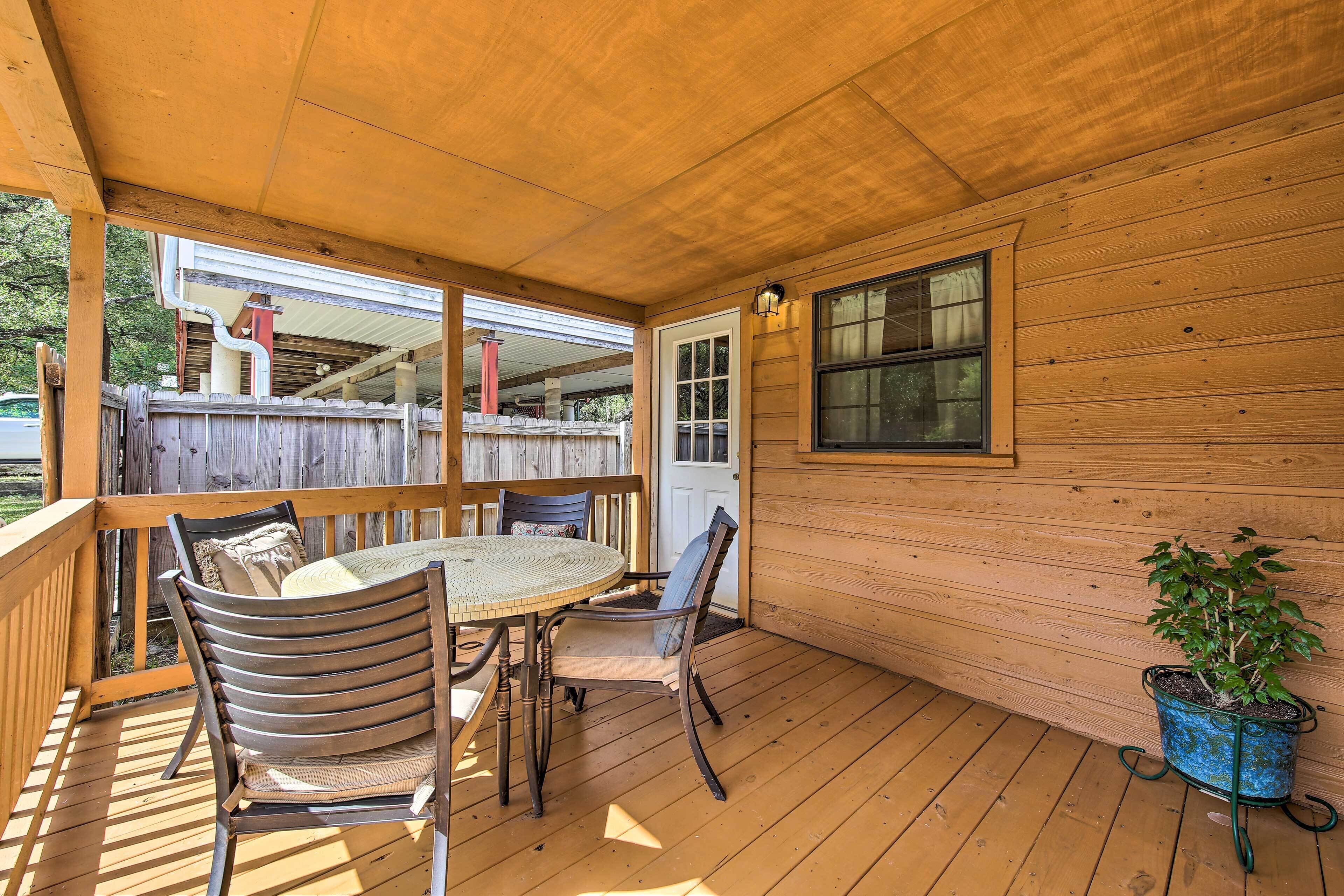 Une terrasse en bois avec une table ronde et des chaises, une plante en pot et une fenêtre.